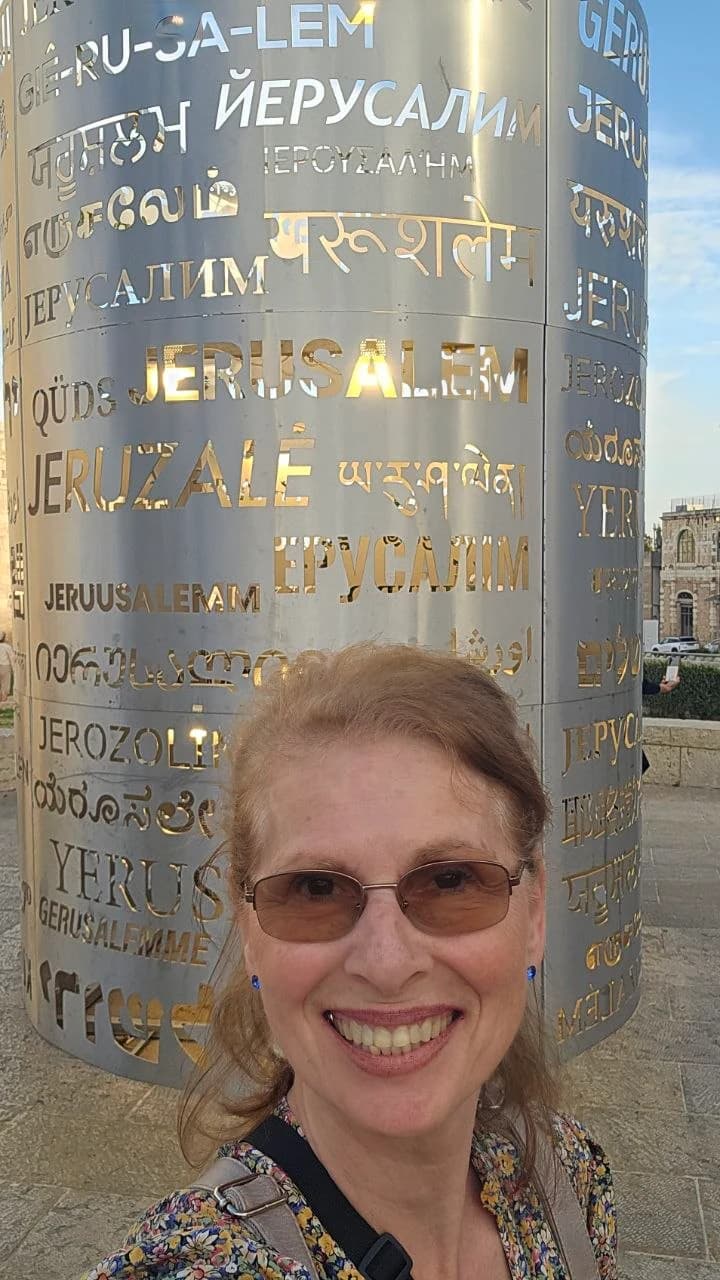 Margaret smiling beside a sculpture bearing Jerusalem's name in many languages